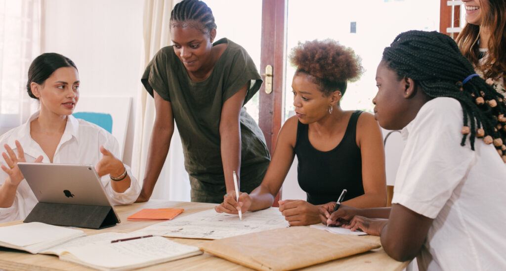A diverse group of five people collaborates around a table with an open laptop and documents, conveying teamwork and focused discussion.
