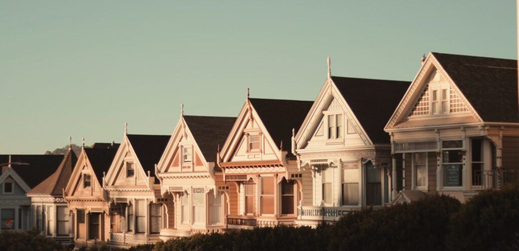 Row of Victorian houses with intricate detailing, bathed in warm sunlight. The sky is clear, creating a calm and nostalgic atmosphere.