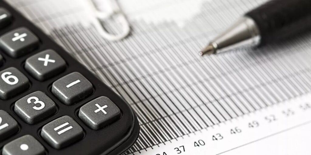 Close-up of a calculator, pen, and paperclip on a striped financial document. The scene conveys an analytical and business-focused tone.