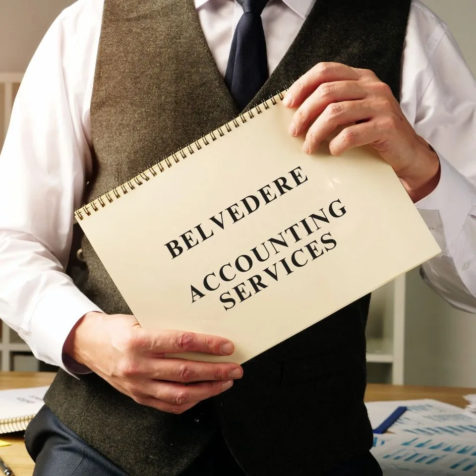 Belvedere A person in a suit holds a spiral-bound notepad titled "Bexleyheath Accounting Services" in an office setting, conveying professionalism and business focus.